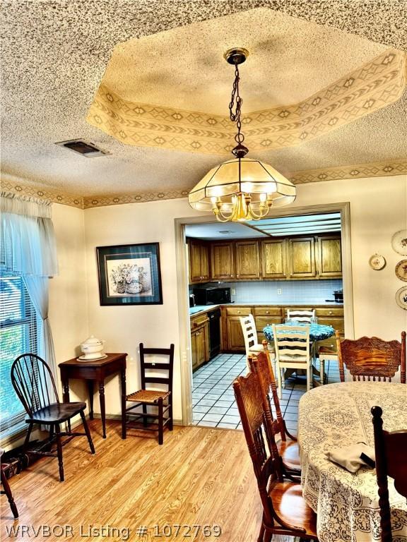 dining space with a chandelier, a textured ceiling, light hardwood / wood-style flooring, and a raised ceiling