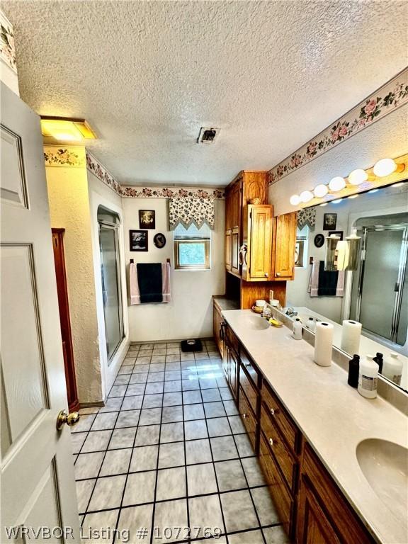 bathroom with a textured ceiling, vanity, tile patterned floors, and walk in shower