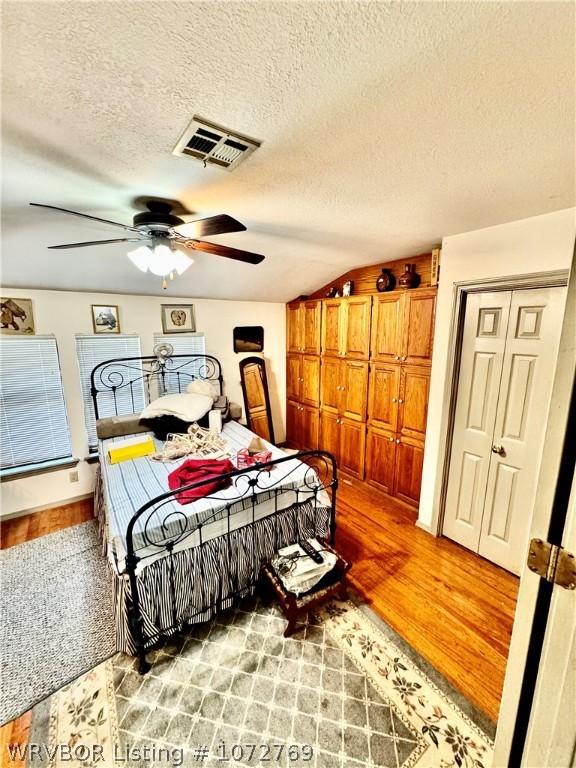 bedroom with hardwood / wood-style floors, a textured ceiling, vaulted ceiling, and ceiling fan