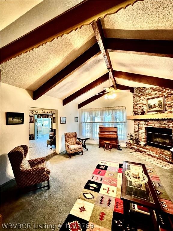 living room featuring lofted ceiling with beams, a brick fireplace, ceiling fan, a textured ceiling, and carpet floors