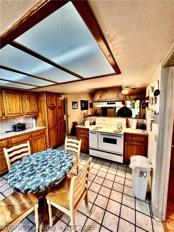 kitchen featuring a textured ceiling, backsplash, light tile patterned flooring, and white stove