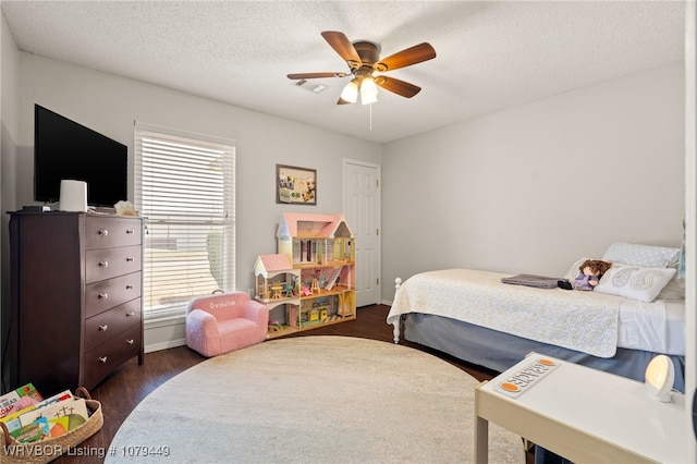 bedroom with baseboards, visible vents, a ceiling fan, dark wood-type flooring, and a textured ceiling