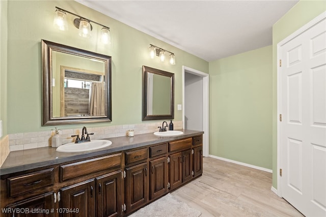 bathroom with double vanity, baseboards, a sink, and wood finished floors