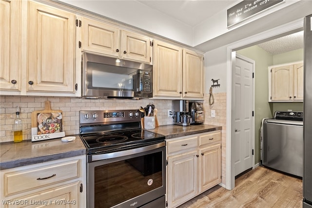 kitchen featuring dark countertops, washer / clothes dryer, decorative backsplash, appliances with stainless steel finishes, and light wood-style floors