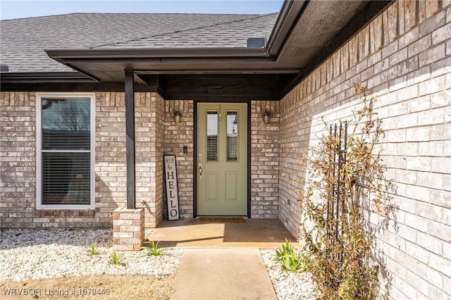 view of exterior entry featuring brick siding and roof with shingles