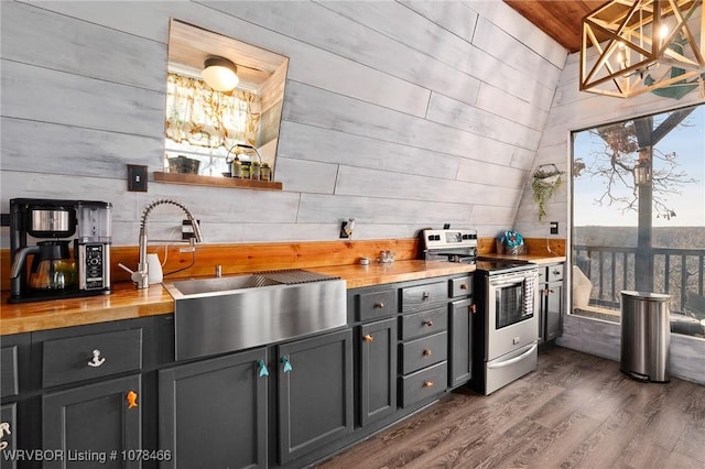 kitchen featuring dark hardwood / wood-style floors, stainless steel electric stove, wood walls, and sink