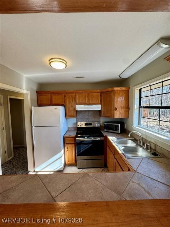 kitchen featuring under cabinet range hood, stainless steel appliances, a sink, and brown cabinetry