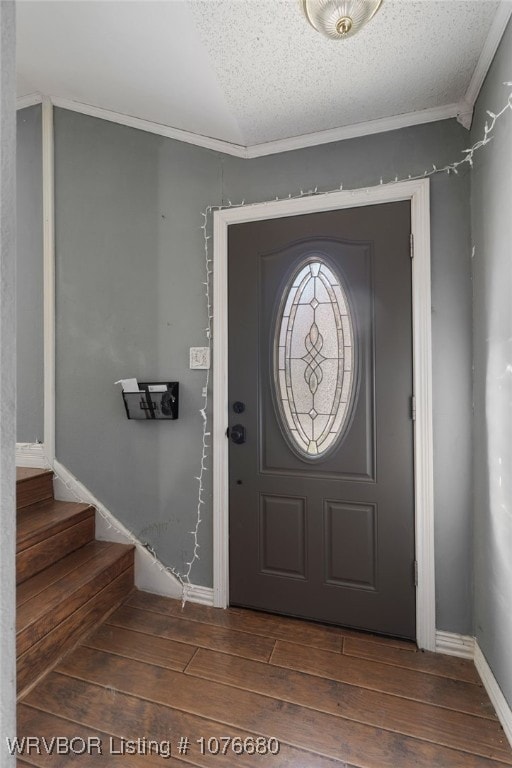 entryway with a textured ceiling, dark wood-type flooring, vaulted ceiling, and ornamental molding