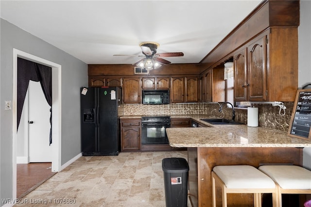 kitchen featuring kitchen peninsula, backsplash, sink, black appliances, and a breakfast bar area