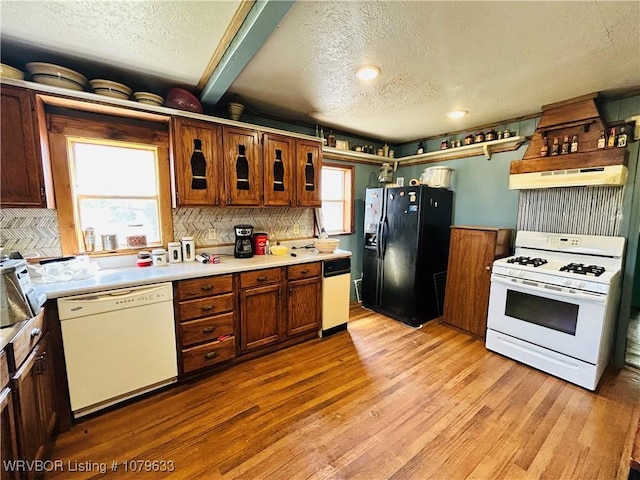 kitchen with under cabinet range hood, light countertops, light wood-type flooring, and white appliances