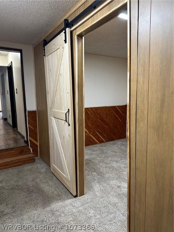 corridor with carpet, a textured ceiling, a barn door, and wood walls