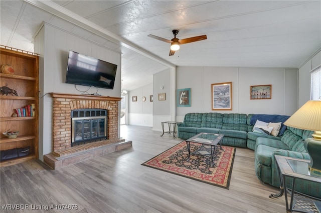 living room with light hardwood / wood-style floors, a brick fireplace, ceiling fan, and lofted ceiling