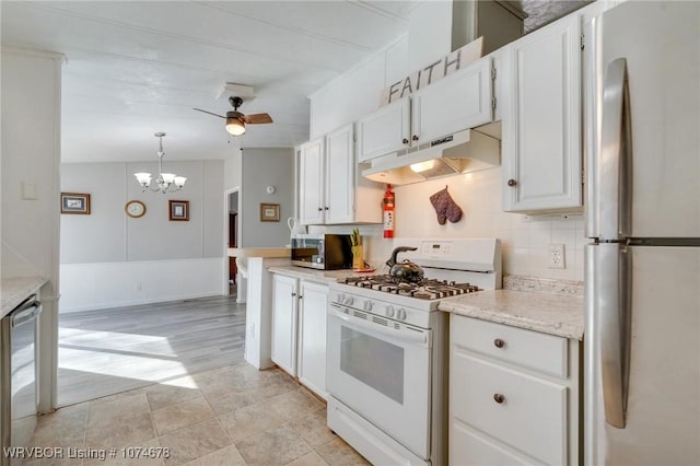 kitchen with appliances with stainless steel finishes, tasteful backsplash, ceiling fan with notable chandelier, white cabinets, and hanging light fixtures