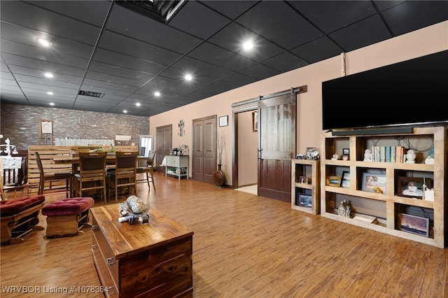 living room featuring hardwood / wood-style floors, a barn door, and brick wall