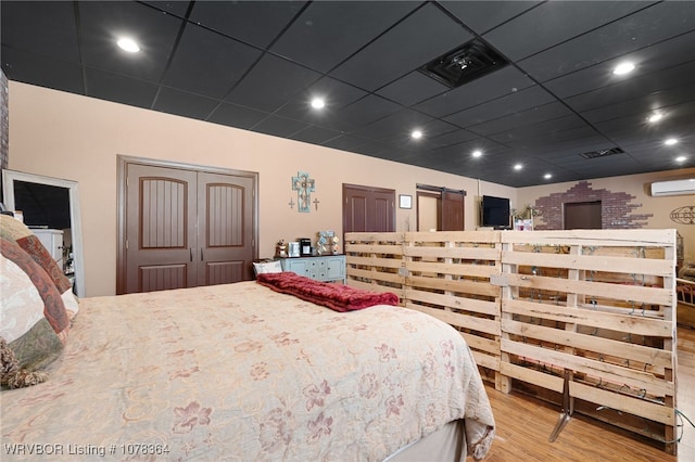 bedroom featuring an AC wall unit, a paneled ceiling, a closet, and light hardwood / wood-style floors