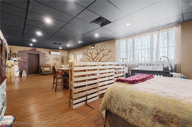 bedroom featuring a paneled ceiling, a wall mounted air conditioner, and hardwood / wood-style flooring