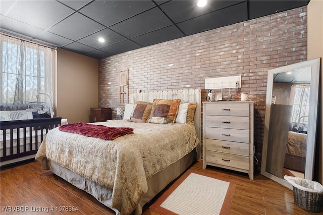 bedroom with a paneled ceiling, hardwood / wood-style floors, and brick wall