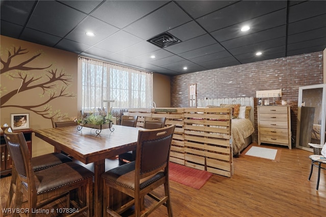 dining space featuring a drop ceiling, wood-type flooring, and brick wall