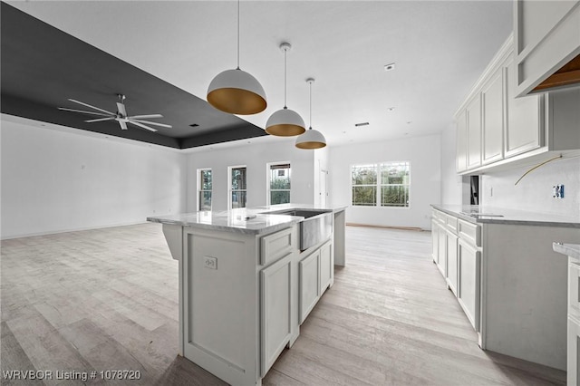 kitchen with white cabinetry, an island with sink, hanging light fixtures, light hardwood / wood-style floors, and a raised ceiling