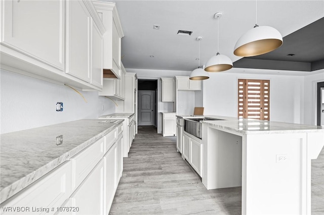 kitchen with pendant lighting, white cabinetry, a center island, light stone counters, and light hardwood / wood-style floors