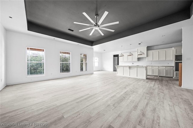 unfurnished living room featuring a raised ceiling, ceiling fan, and light hardwood / wood-style flooring