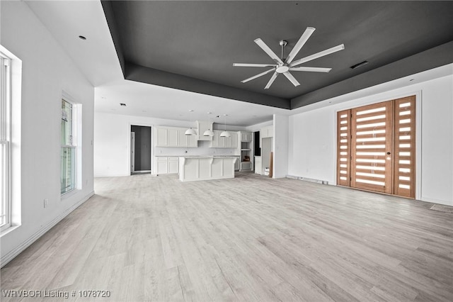 unfurnished living room with a raised ceiling, ceiling fan, and light wood-type flooring