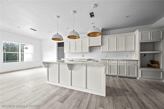 kitchen featuring hanging light fixtures, an island with sink, light stone countertops, and gray cabinets