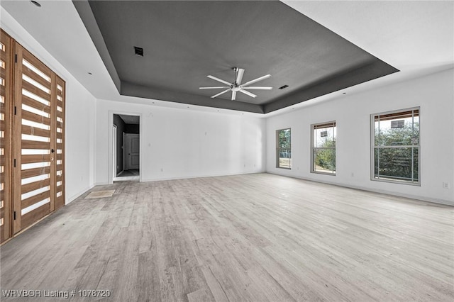 unfurnished living room featuring light hardwood / wood-style flooring, ceiling fan, and a tray ceiling