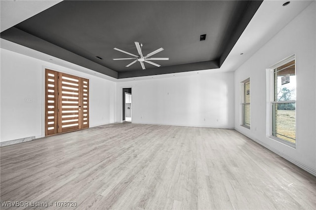 unfurnished living room featuring ceiling fan, light wood-type flooring, and a tray ceiling