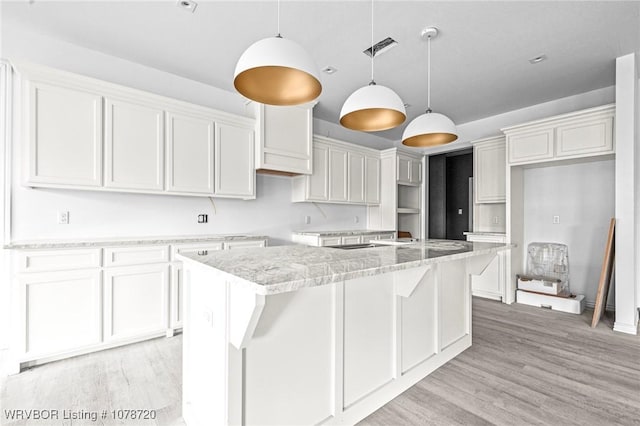 kitchen featuring white cabinetry, decorative light fixtures, light stone counters, and a kitchen island