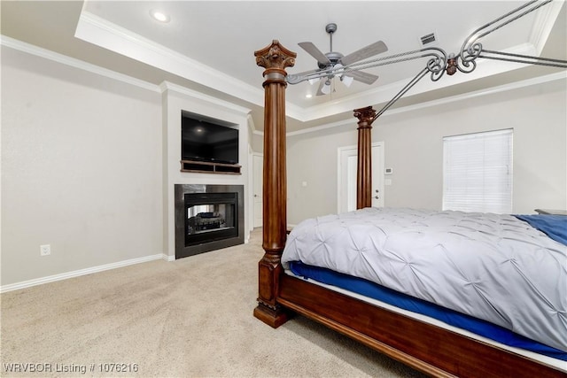 bedroom with ceiling fan, a multi sided fireplace, a raised ceiling, crown molding, and light colored carpet