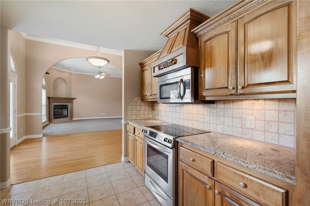 kitchen featuring light stone counters, stainless steel appliances, ceiling fan, crown molding, and light tile patterned floors