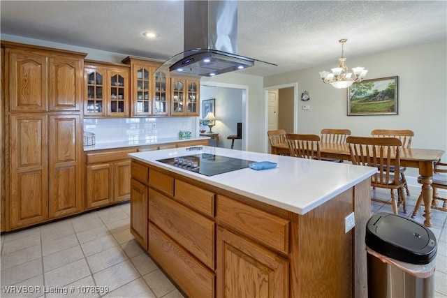 kitchen featuring hanging light fixtures, tasteful backsplash, island range hood, a kitchen island, and black electric cooktop