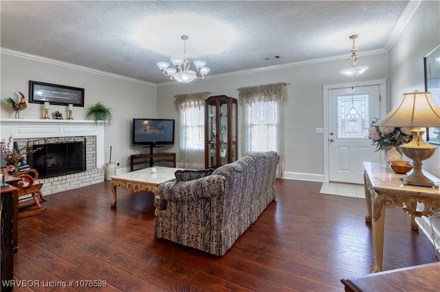 living room with a fireplace, a chandelier, ornamental molding, dark wood-type flooring, and a textured ceiling