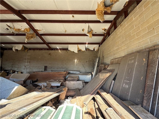 miscellaneous room with beamed ceiling and brick wall