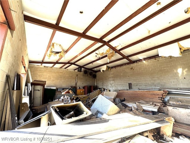 misc room featuring vaulted ceiling with beams and brick wall