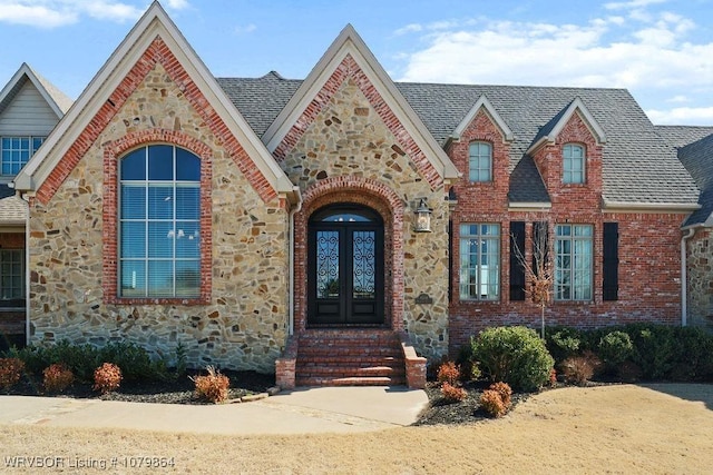 view of front of home featuring french doors, stone siding, brick siding, and a shingled roof