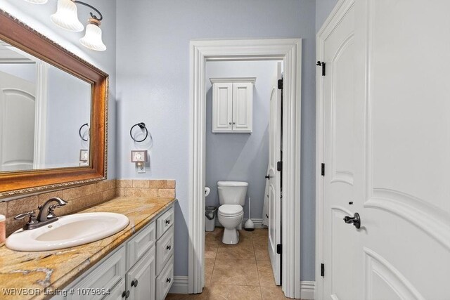 bathroom featuring tile patterned floors, toilet, vanity, tasteful backsplash, and baseboards