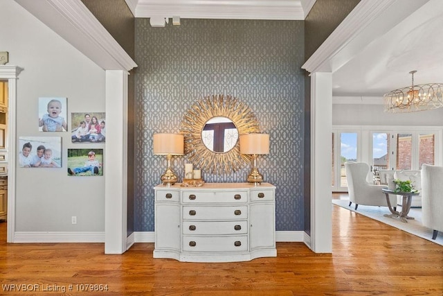hall featuring crown molding, baseboards, wallpapered walls, wood finished floors, and a notable chandelier