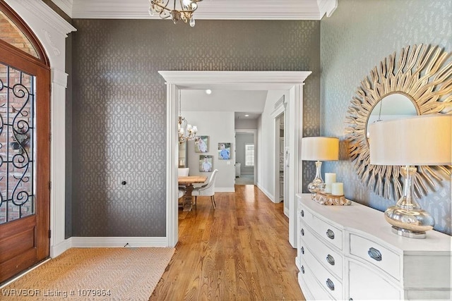 foyer with crown molding, baseboards, wallpapered walls, and a notable chandelier