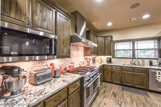 kitchen featuring sink, wall chimney exhaust hood, stainless steel appliances, dark brown cabinets, and light wood-type flooring