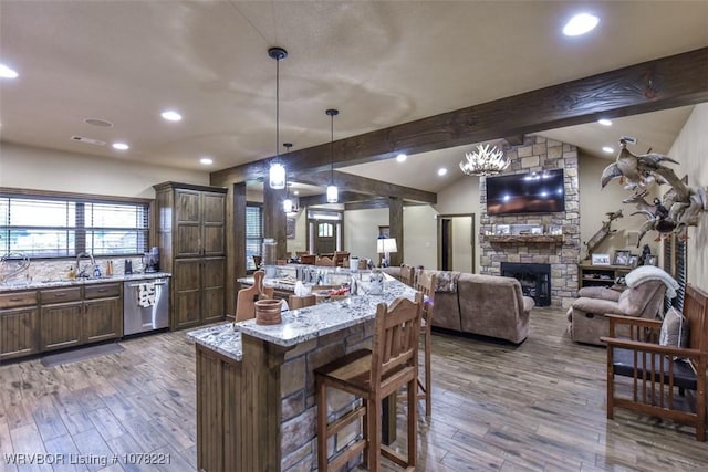 kitchen featuring pendant lighting, dishwasher, a stone fireplace, light stone countertops, and a kitchen bar