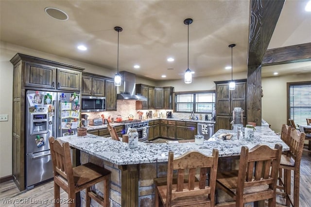 kitchen featuring decorative light fixtures, a spacious island, wall chimney range hood, and stainless steel appliances