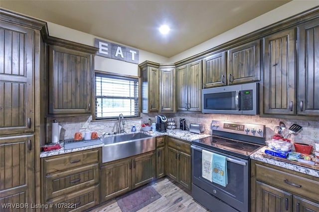 kitchen featuring dark brown cabinetry, light stone countertops, sink, light hardwood / wood-style flooring, and appliances with stainless steel finishes