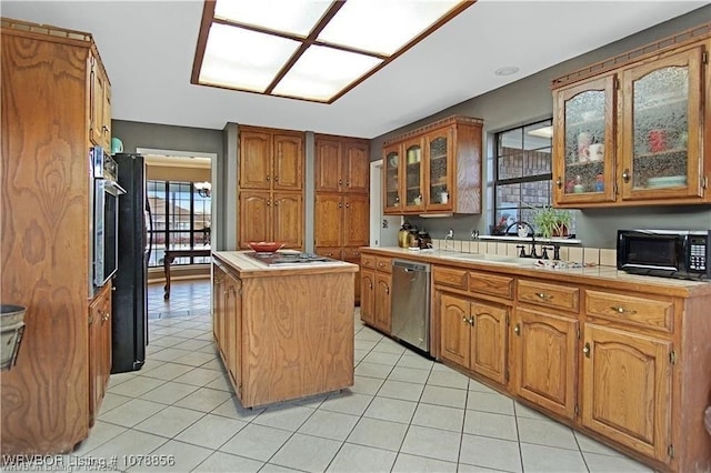 kitchen with a kitchen island, sink, tile counters, light tile patterned floors, and black appliances