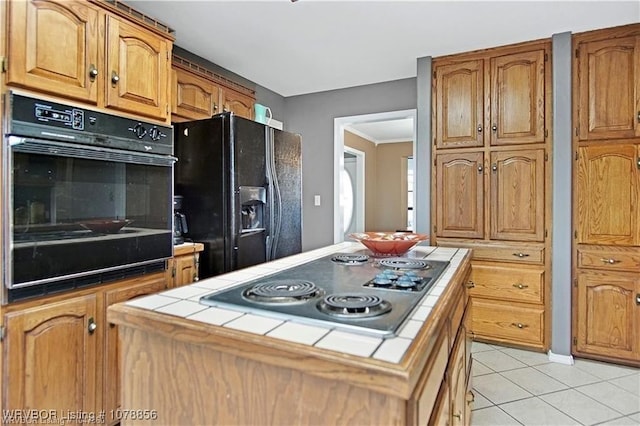 kitchen with light tile patterned floors, tile counters, black appliances, and a center island