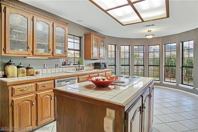 kitchen with light tile patterned floors, sink, a center island, tile countertops, and stainless steel dishwasher