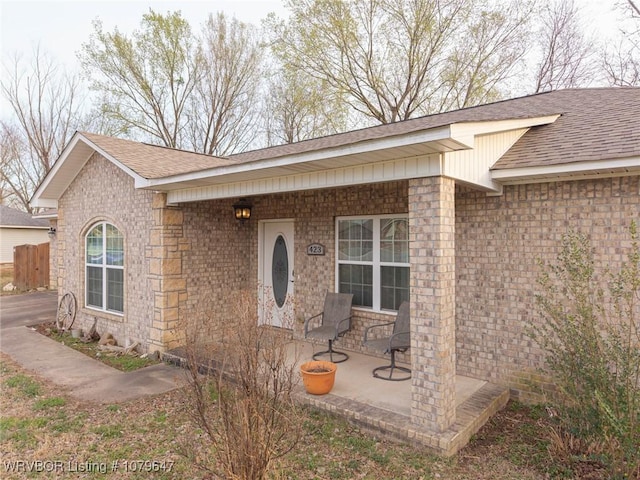 view of exterior entry with a porch, brick siding, and a shingled roof