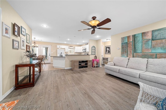 living room featuring recessed lighting, ceiling fan with notable chandelier, baseboards, and light wood finished floors