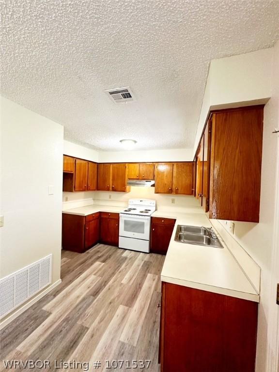 kitchen with electric range, light wood-type flooring, sink, and a textured ceiling